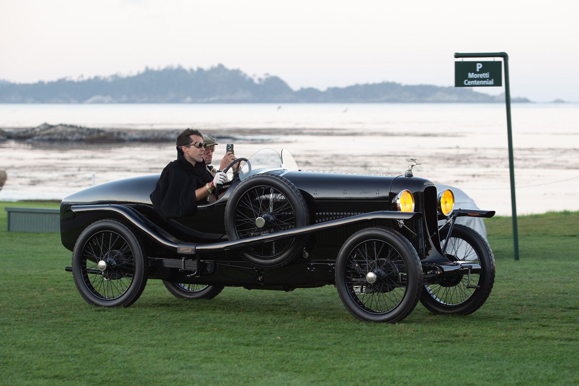 1925 Amilcar CGS Grand Sport, side view, driving on the grass at Pebble Beach Concours with the ocean behind it