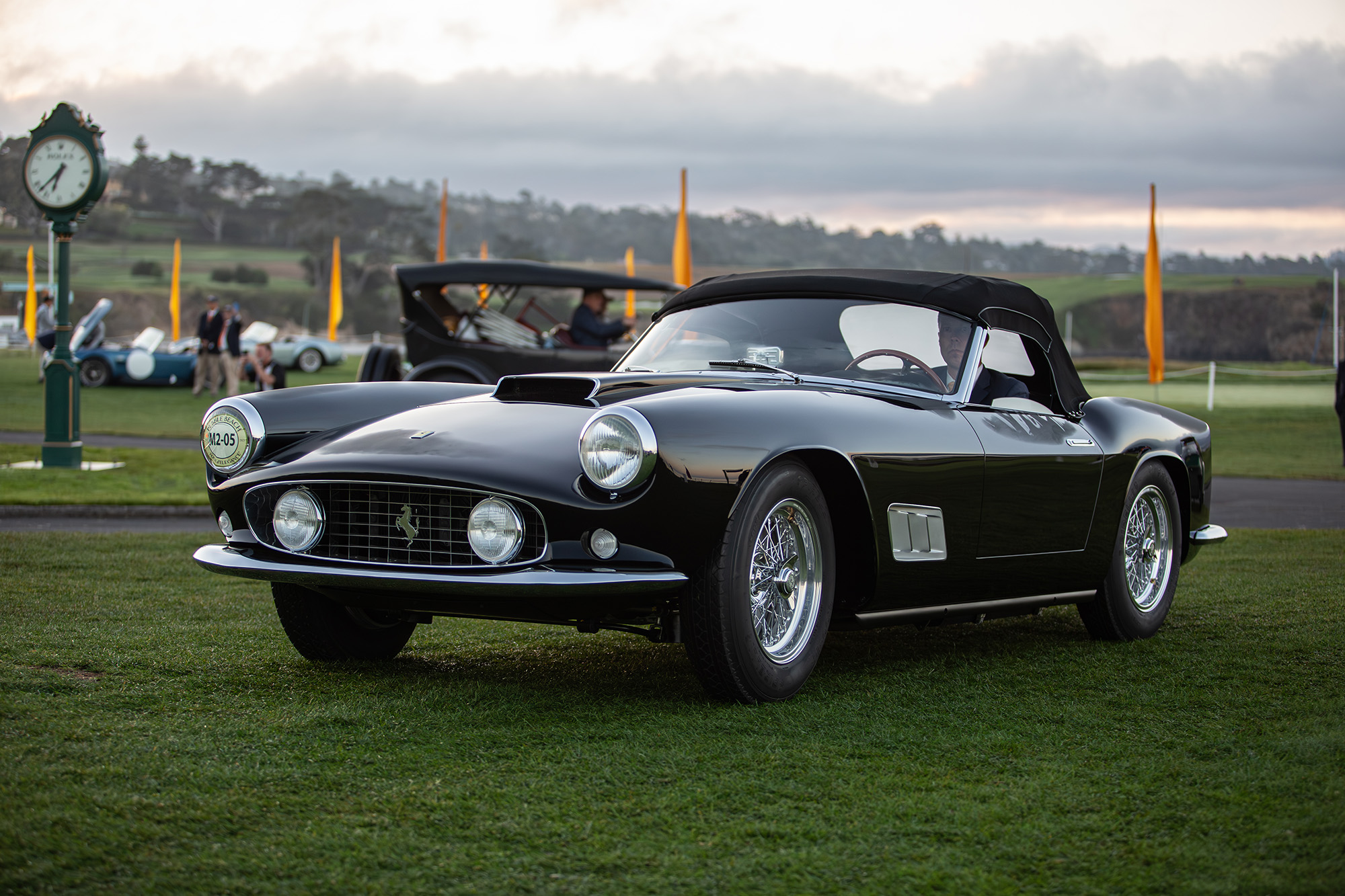 1959 Ferrari 250 GT Spyder California, front quarter, black, driving on the grass at Pebble Beach with the top up