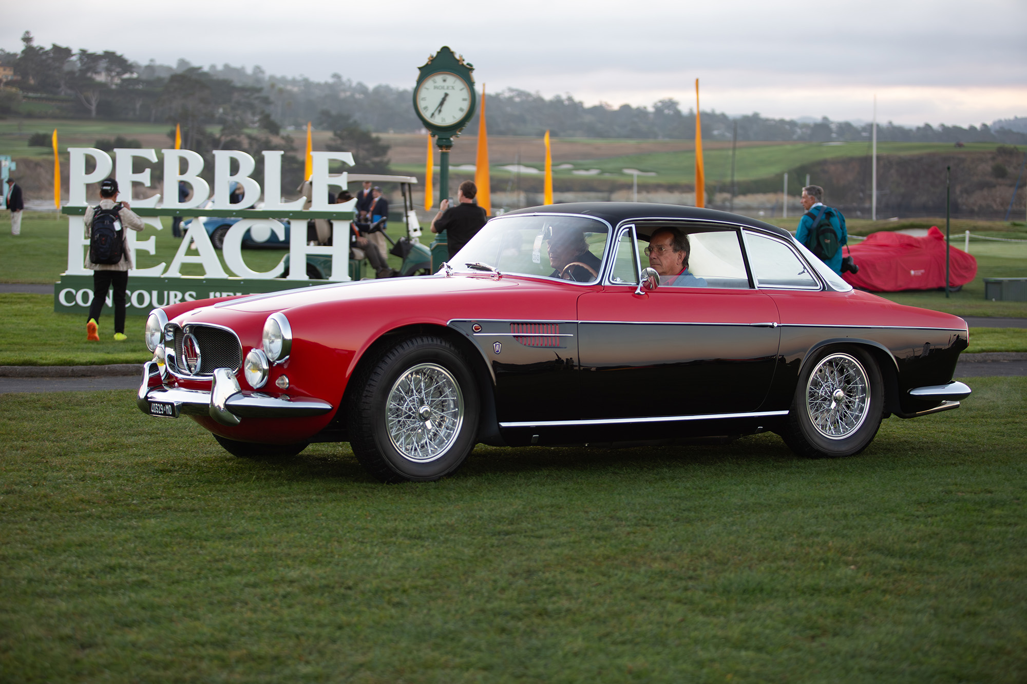 1956 Maserati A6G 2000 Coupe, side view, entering the lawn at Pebble Beach with Pebble Beach sign behind it.