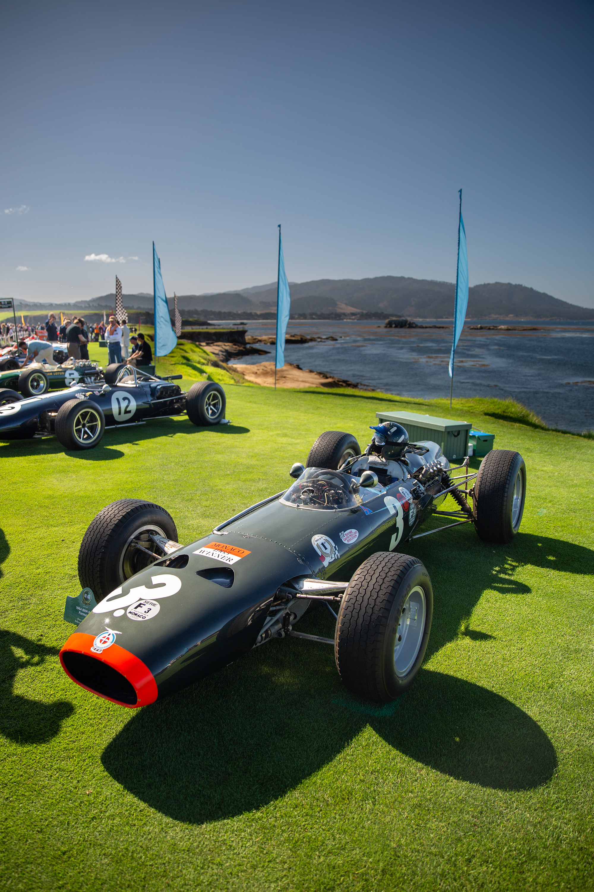 1964 BRM P261, front quarter, with other contemporary F1 cars near it and the ocean at Pebble Beach behind it